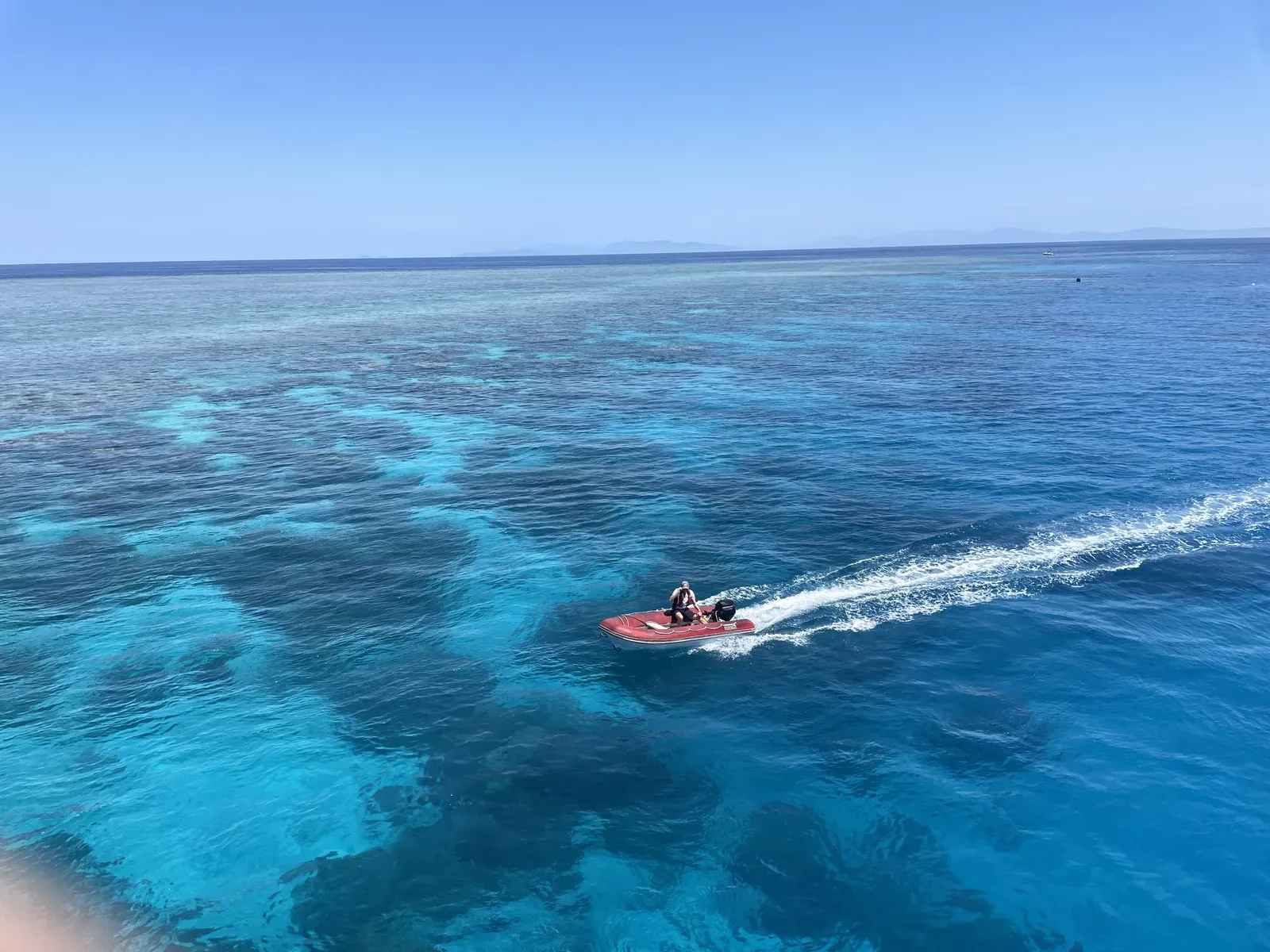 Small motorboat crossing a shallow reef in clear turquoise water.