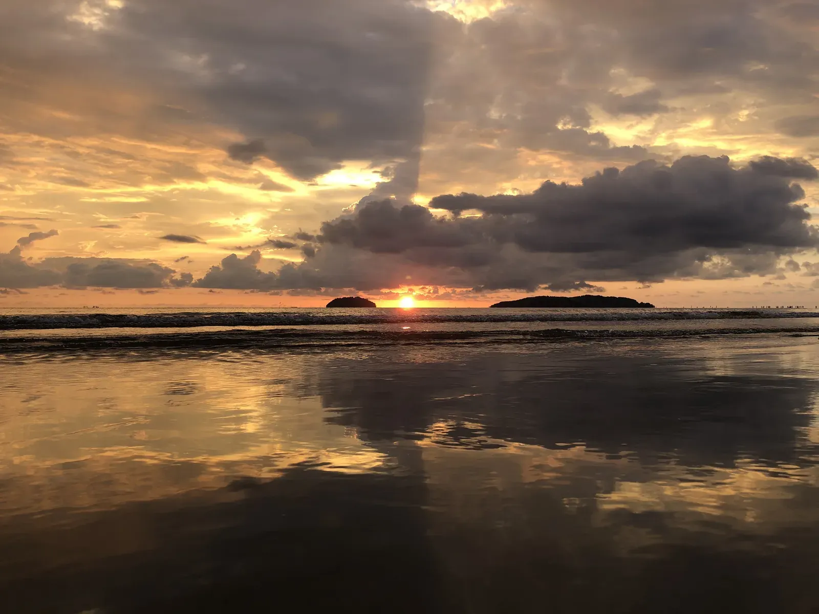 Sun setting between two islands, light spilling across wet sand.
