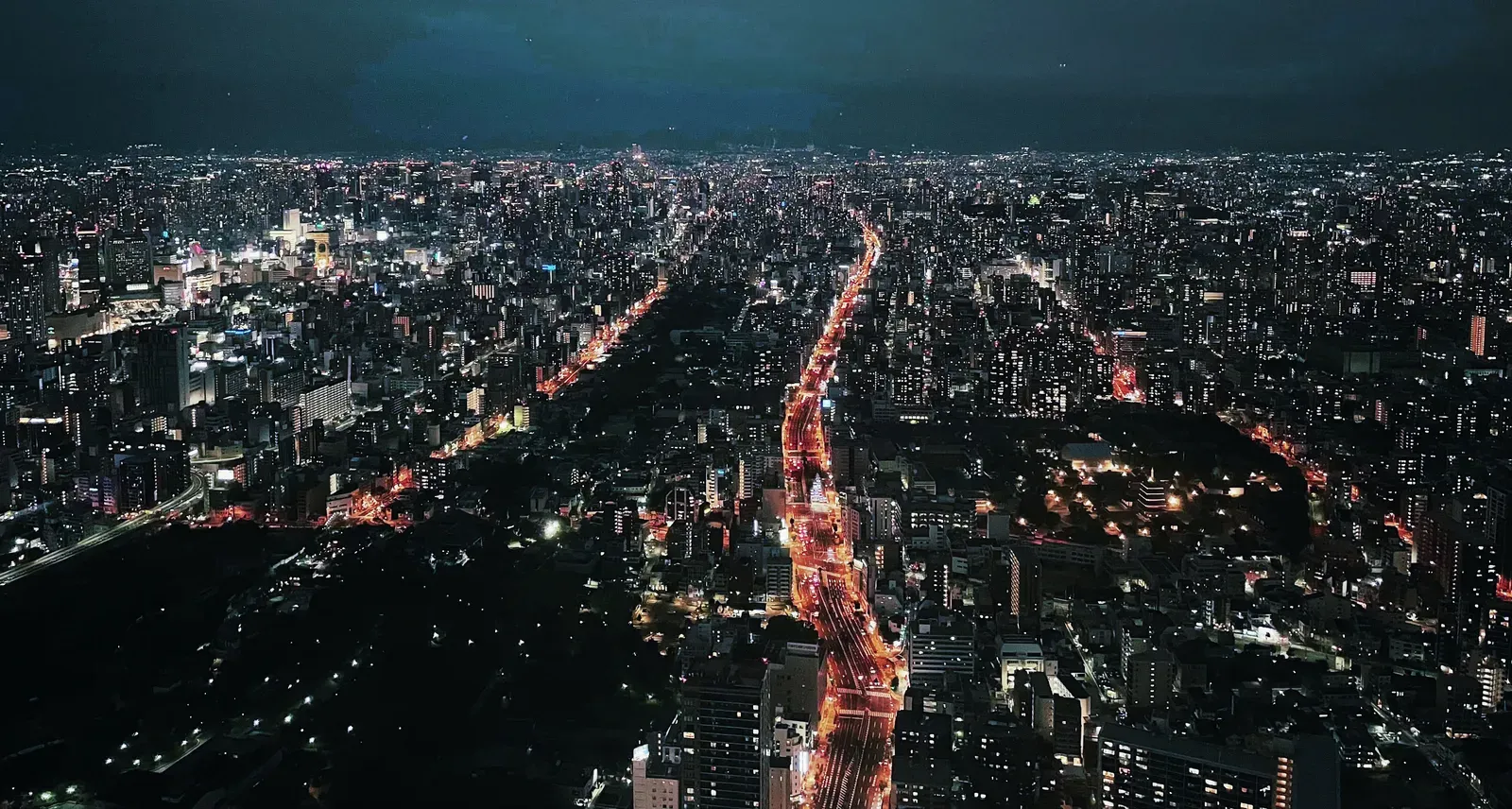Sprawling night city with one bright avenue running through it.